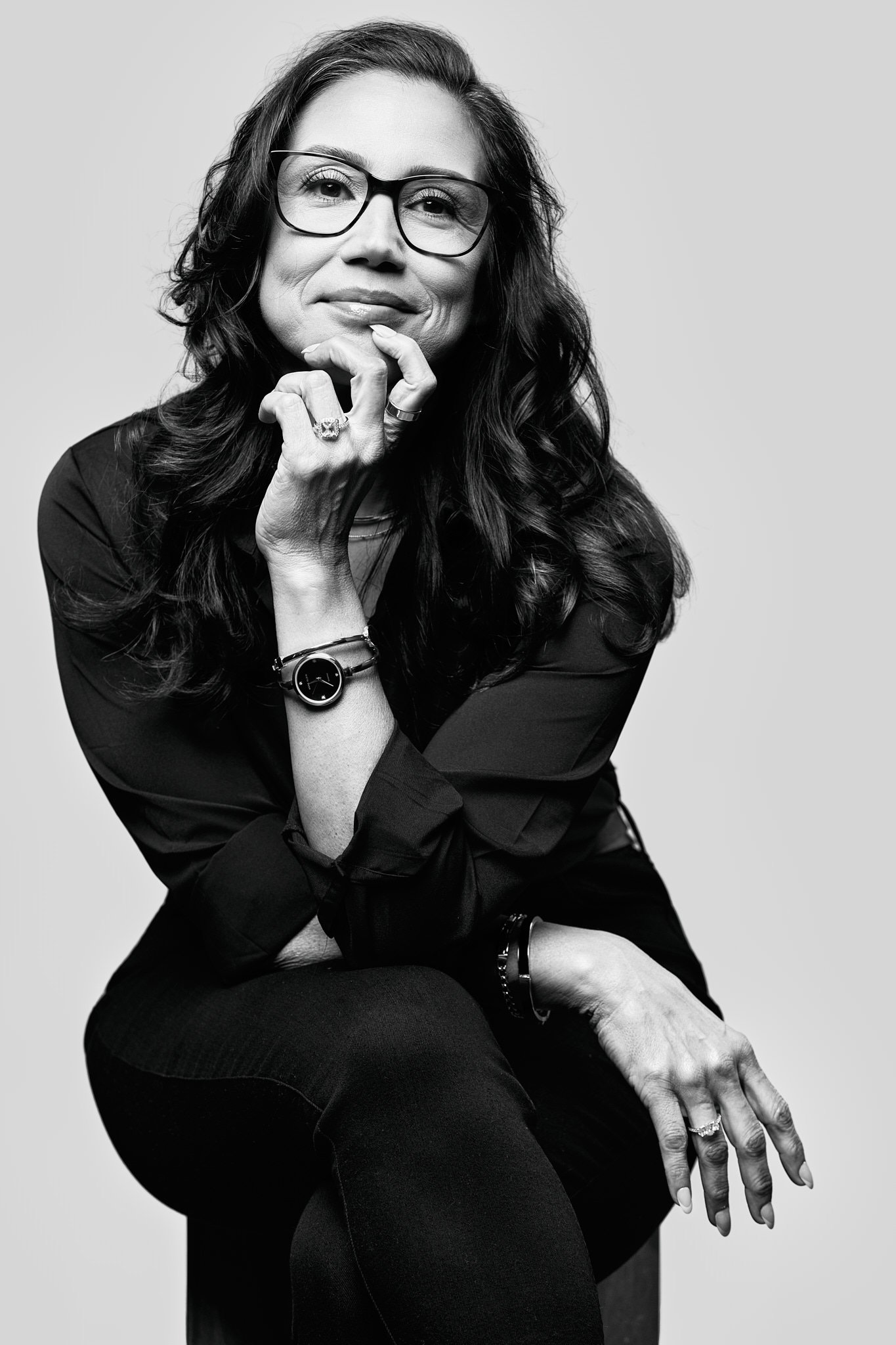 Black and white portrait of a woman in glasses seated, her hand at her chin