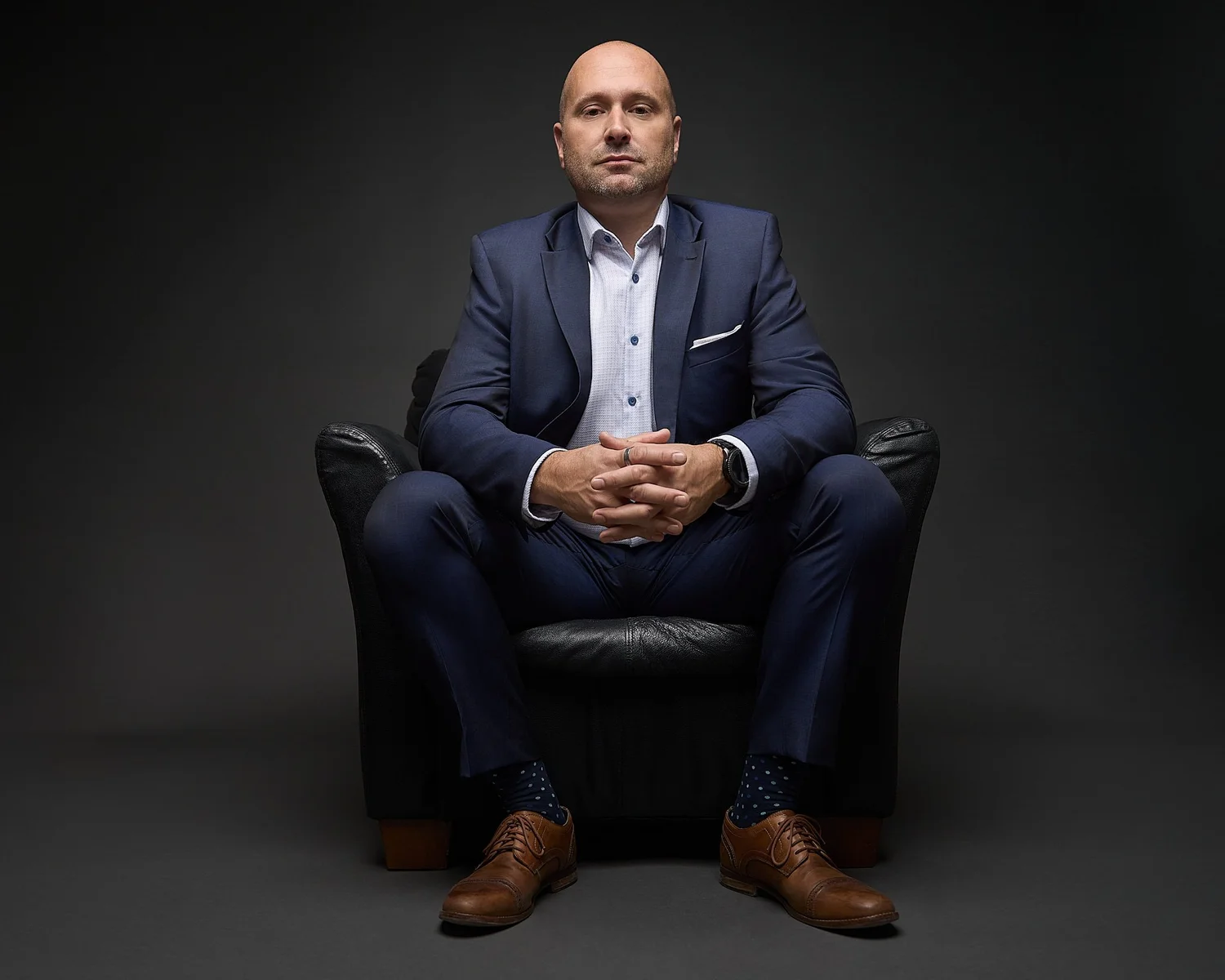 Color portrait of a man in a navy suit seated in a black leather armchair