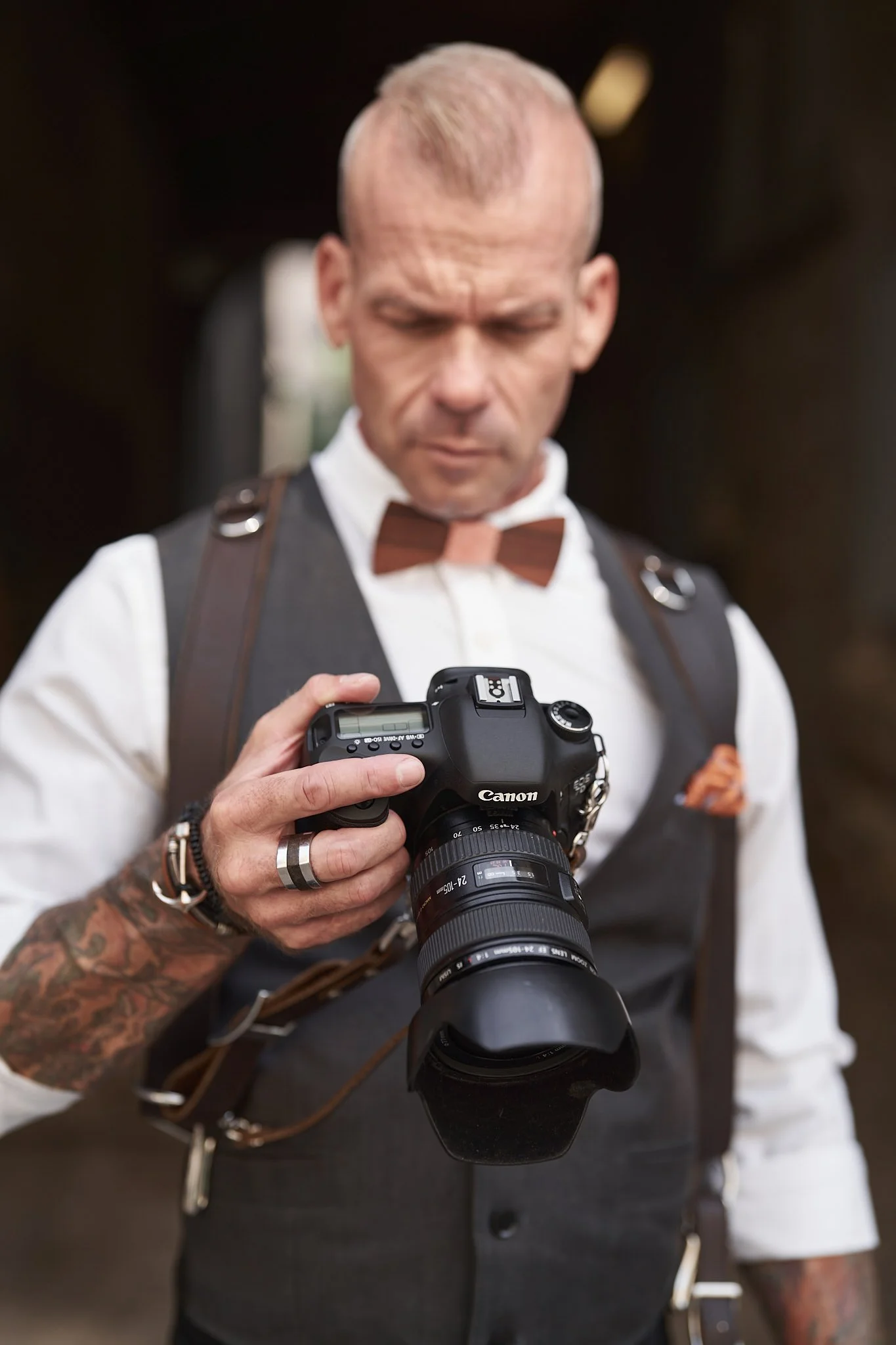 A photographer in a waistcoat and bow tie looking down at his camera on an Ikonic Leather Works harness