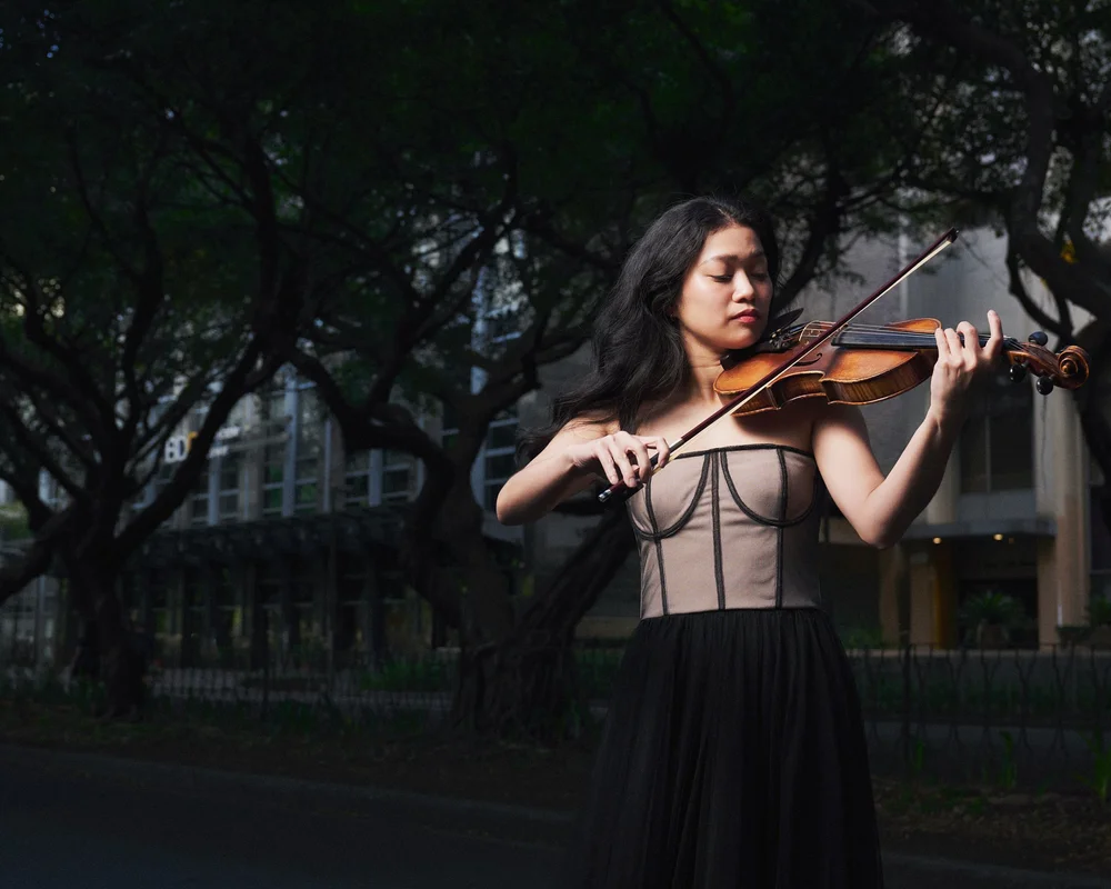 Eliza, a violinist, playing on a city street under dark trees