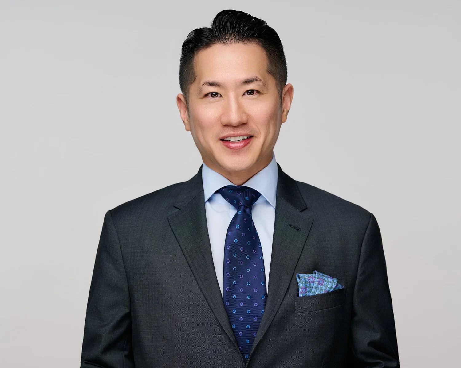 Color headshot of a man in a navy suit on a light grey ground