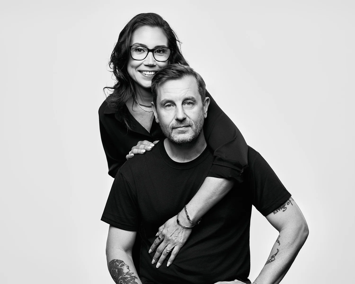 The two owners of Koopers Whiskey together, she leans over his shoulders, black and white on a white backdrop