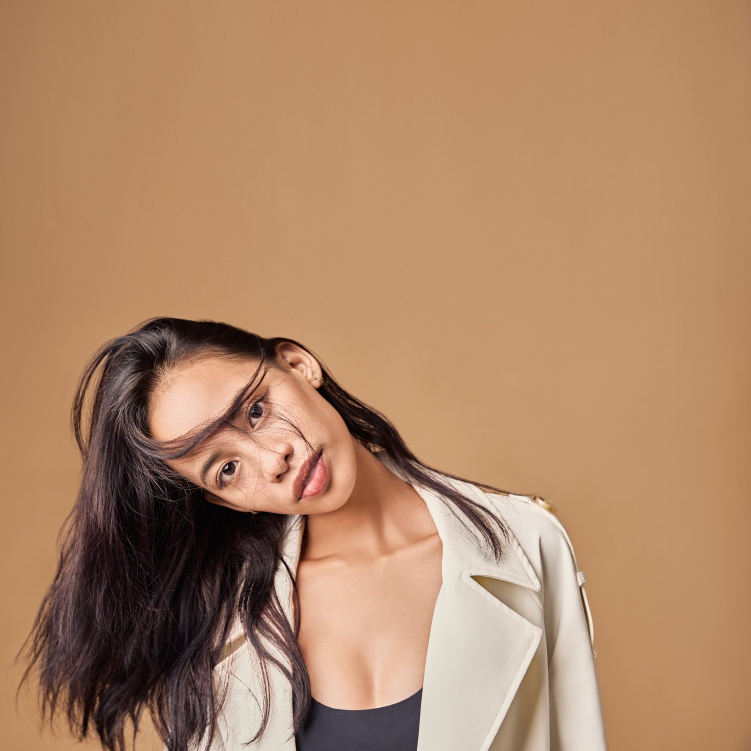 Ash, recording artist, head tilted, hair across her face, on a tan background