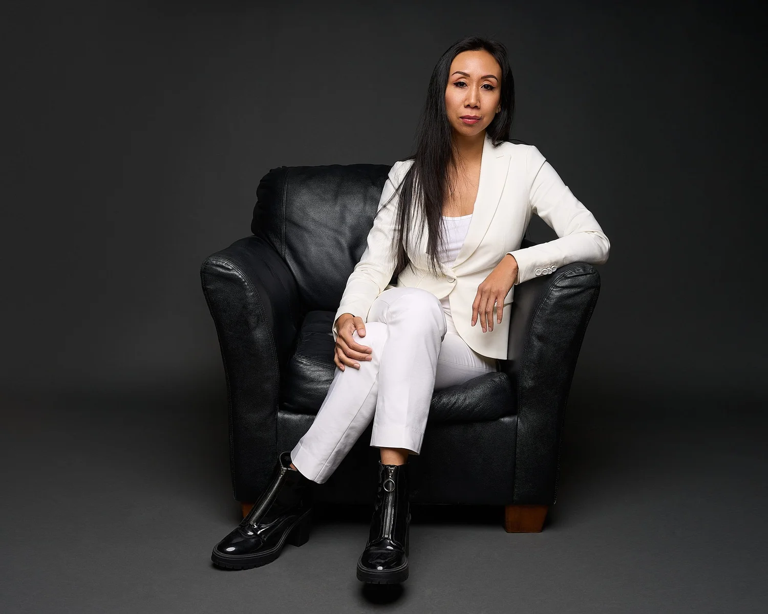 Color portrait of a woman in a white suit seated in a black leather armchair