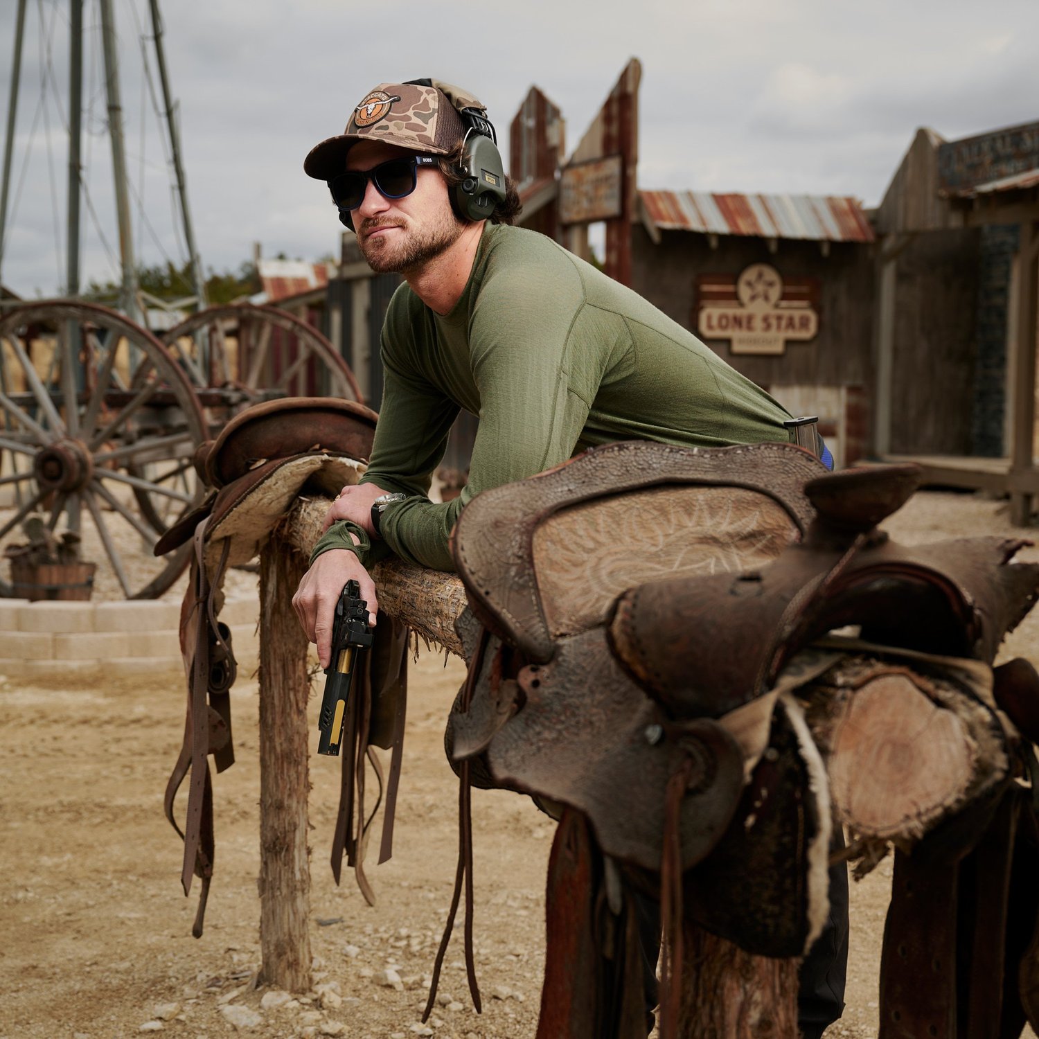Competitive shooter for Staccato in a cap and ear protection, leaning on saddles at an outdoor range