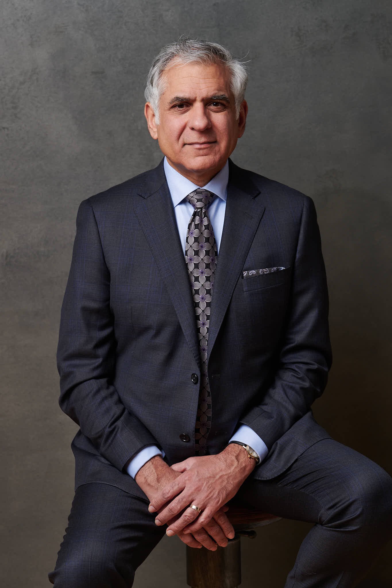 Color portrait of a senior man in a grey suit seated on a dark ground