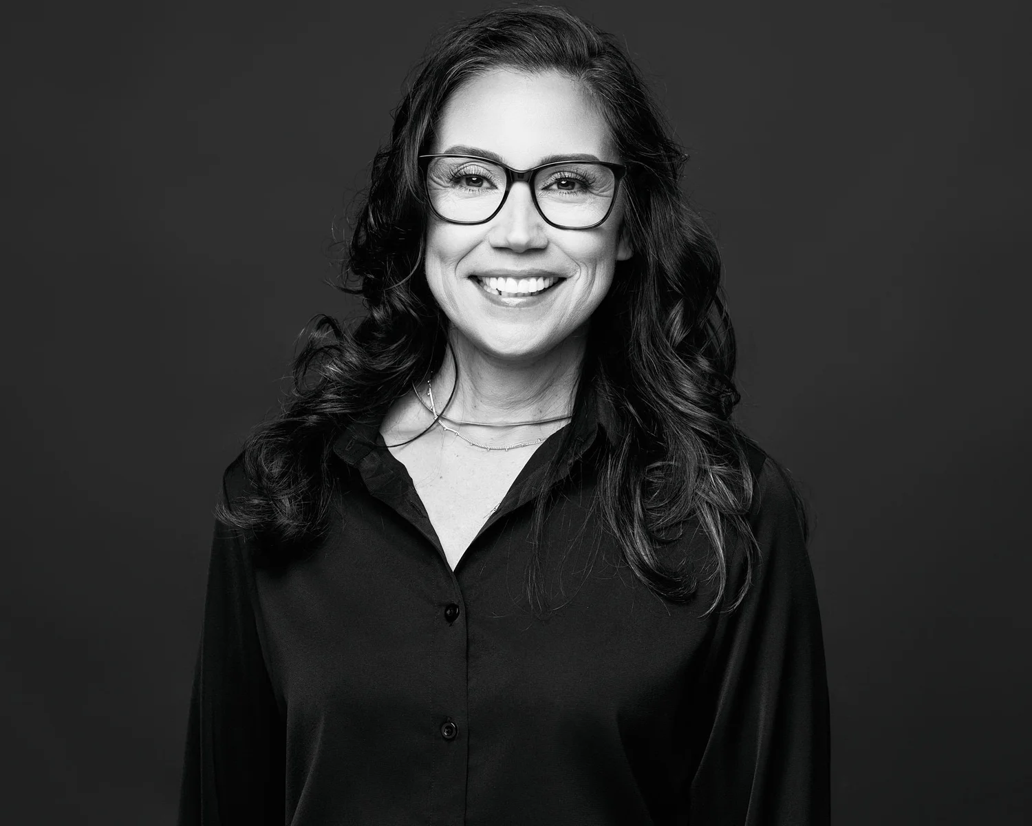 The other owner of Koopers Whiskey, smiling, in glasses, black and white studio portrait on a dark backdrop