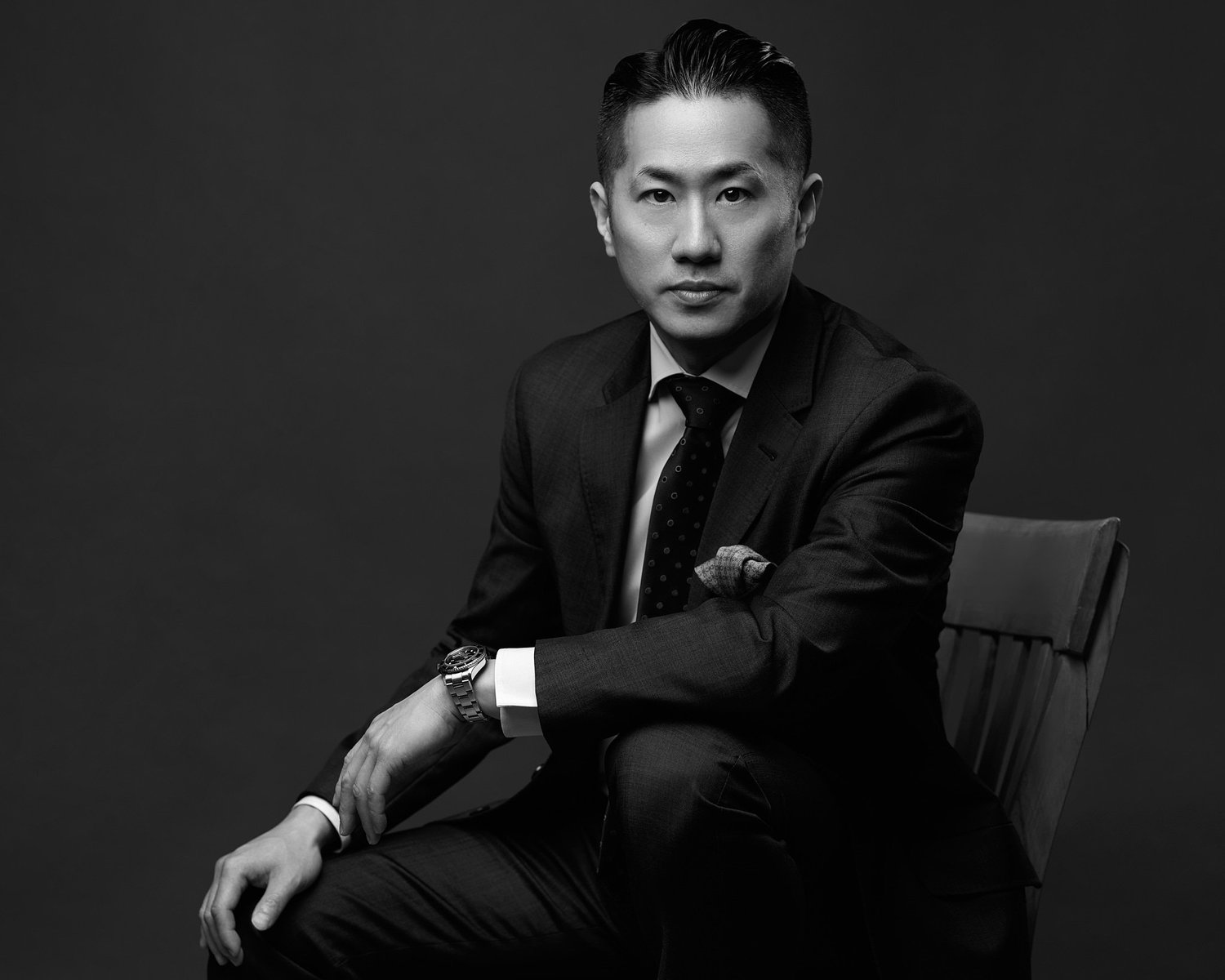 Black and white portrait of a man in a suit seated beside a chair, landscape