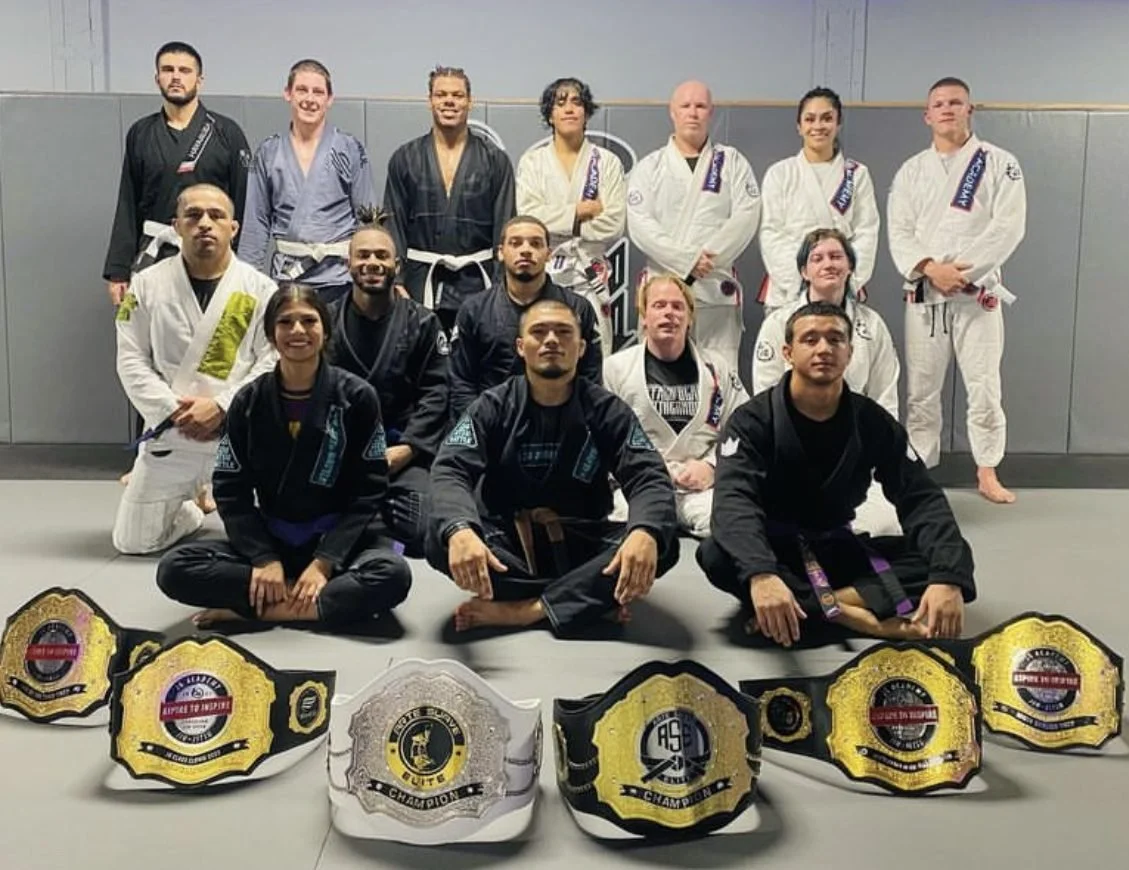 The JG Academy team seated behind a row of championship belts
