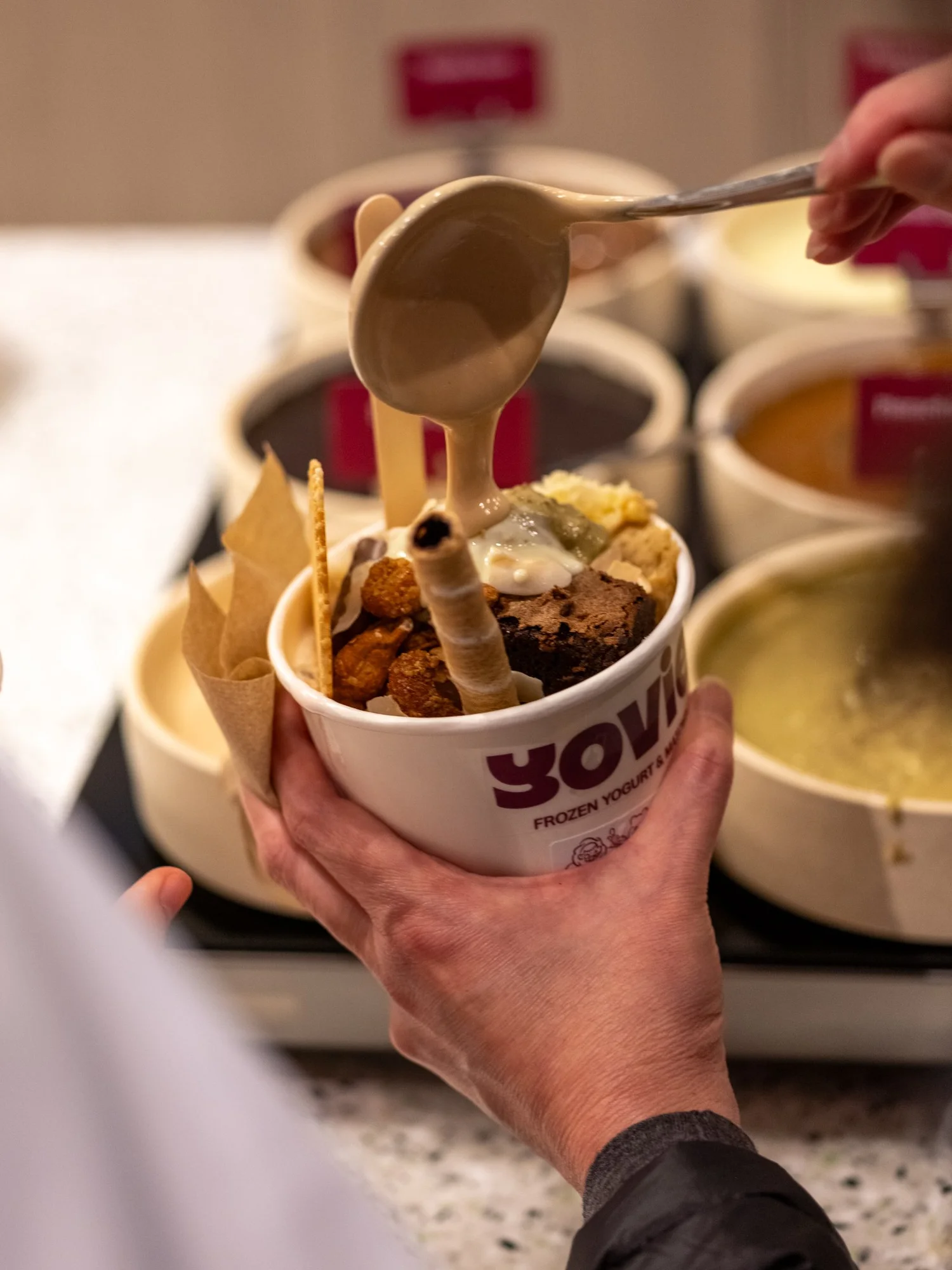 Sauce being poured over a Yovie frozen yoghurt cup
