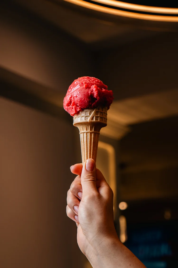 A hand holding a berry-colored gelato cone inside Florenza