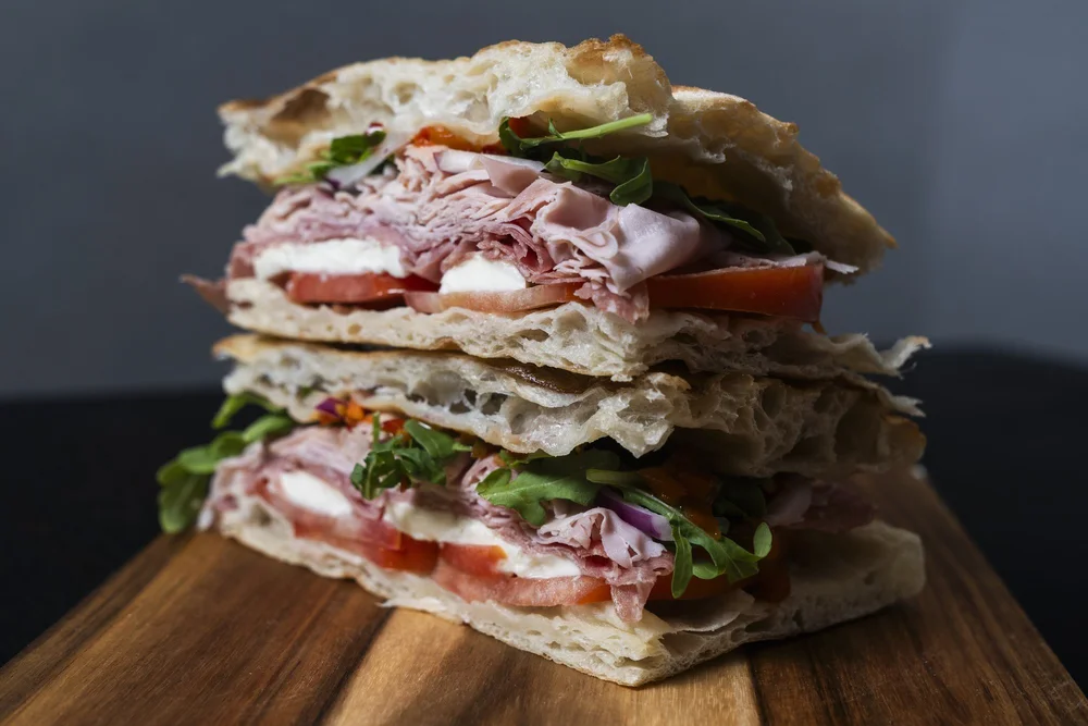 Stacked Florenza panini showing airy bread, sliced meat, cheese, tomato, and greens
