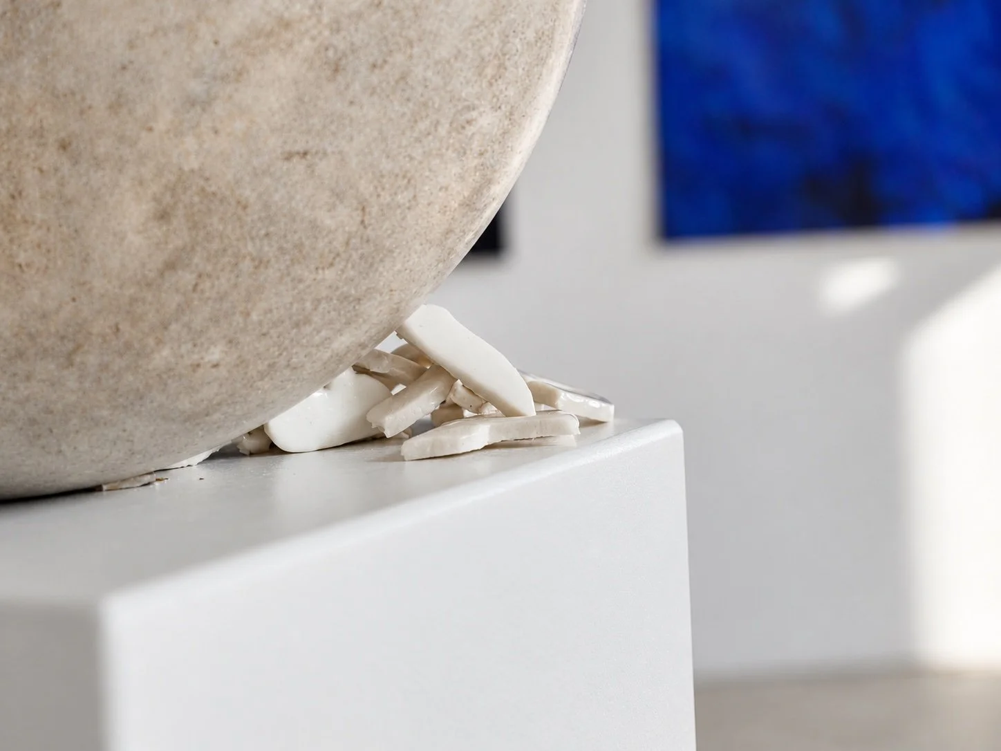 Close view of white porcelain fragments resting against the concrete sphere, with a blue painting blurred behind.