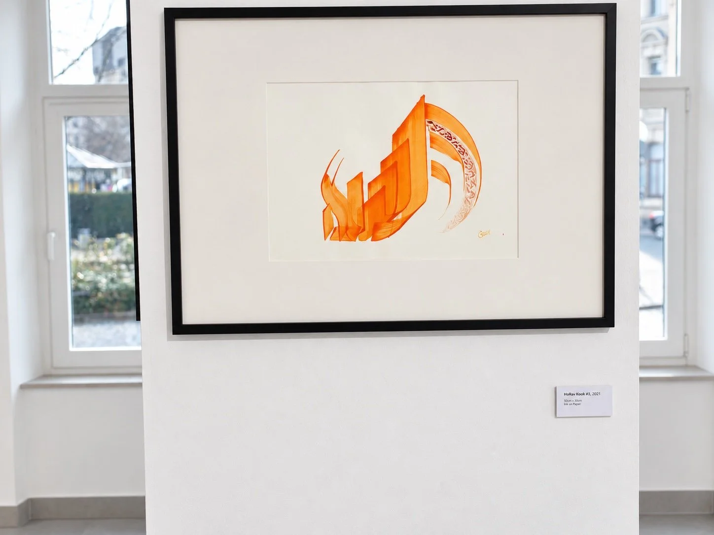 A framed orange calligraphic work with a black frame between two windows, with a small label below.