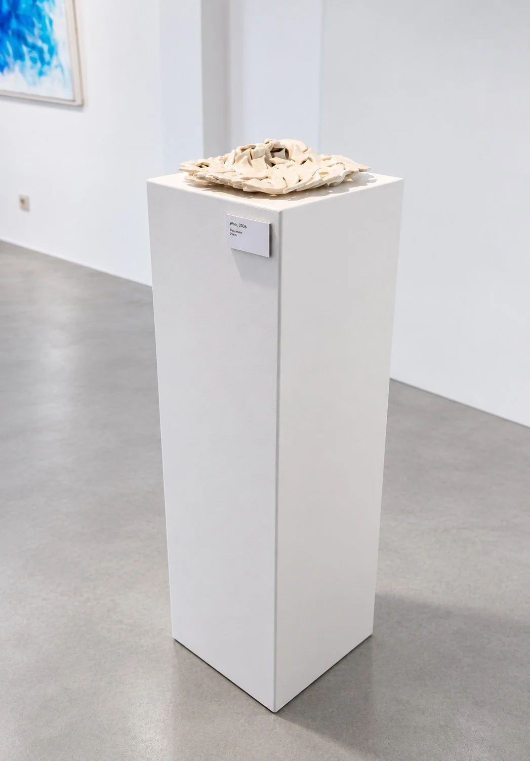 A porcelain sculpture of layered Hebrew letter forms on a tall white plinth with a small label, in a bright gallery.