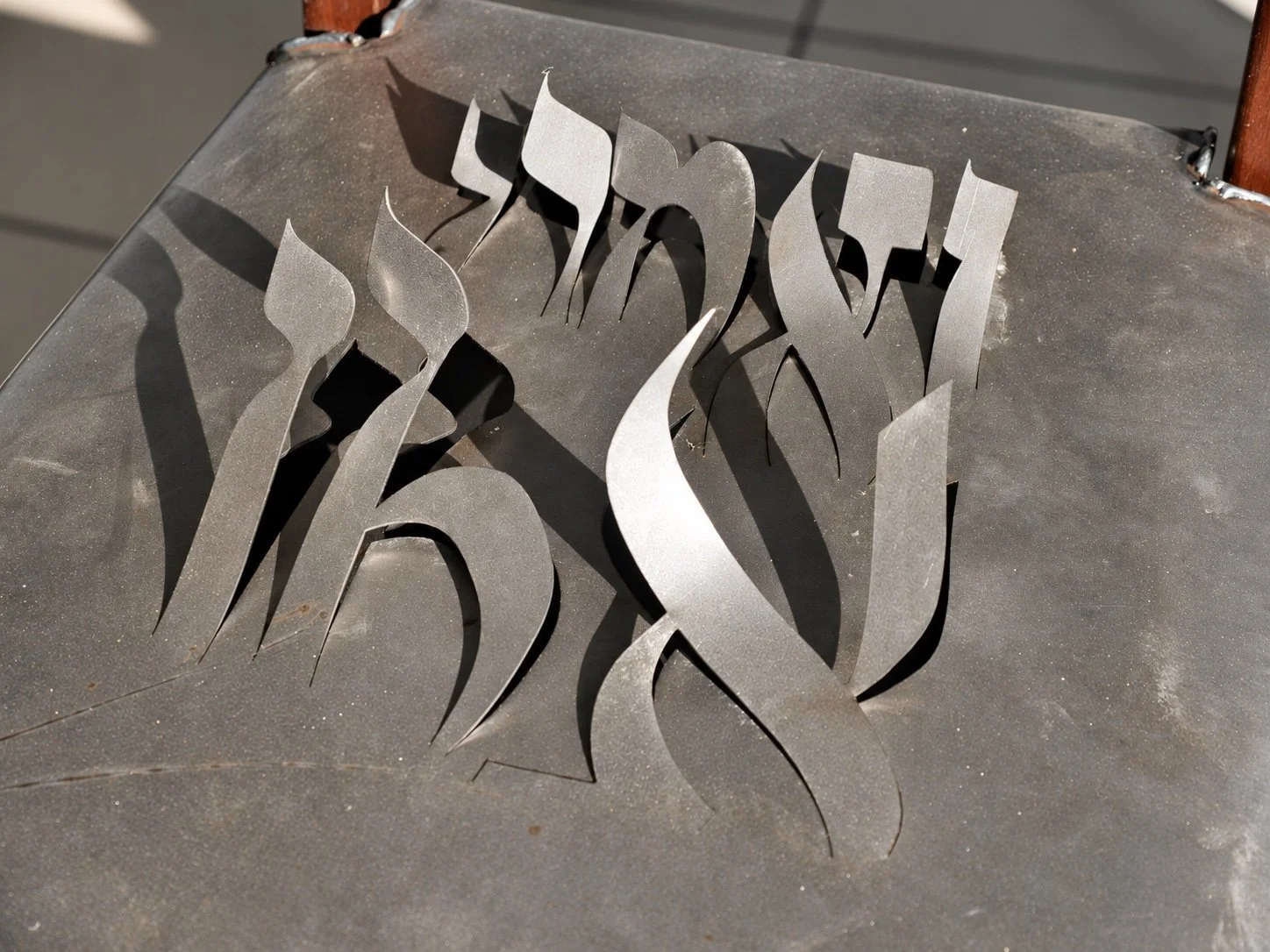 Close view of cut steel letter forms rising from a chair seat.