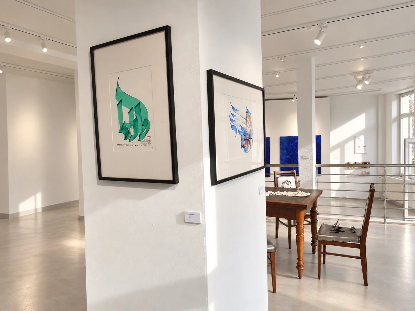 A framed green calligraphic work on a white column; blue paintings and a chair visible beyond the stair railing.