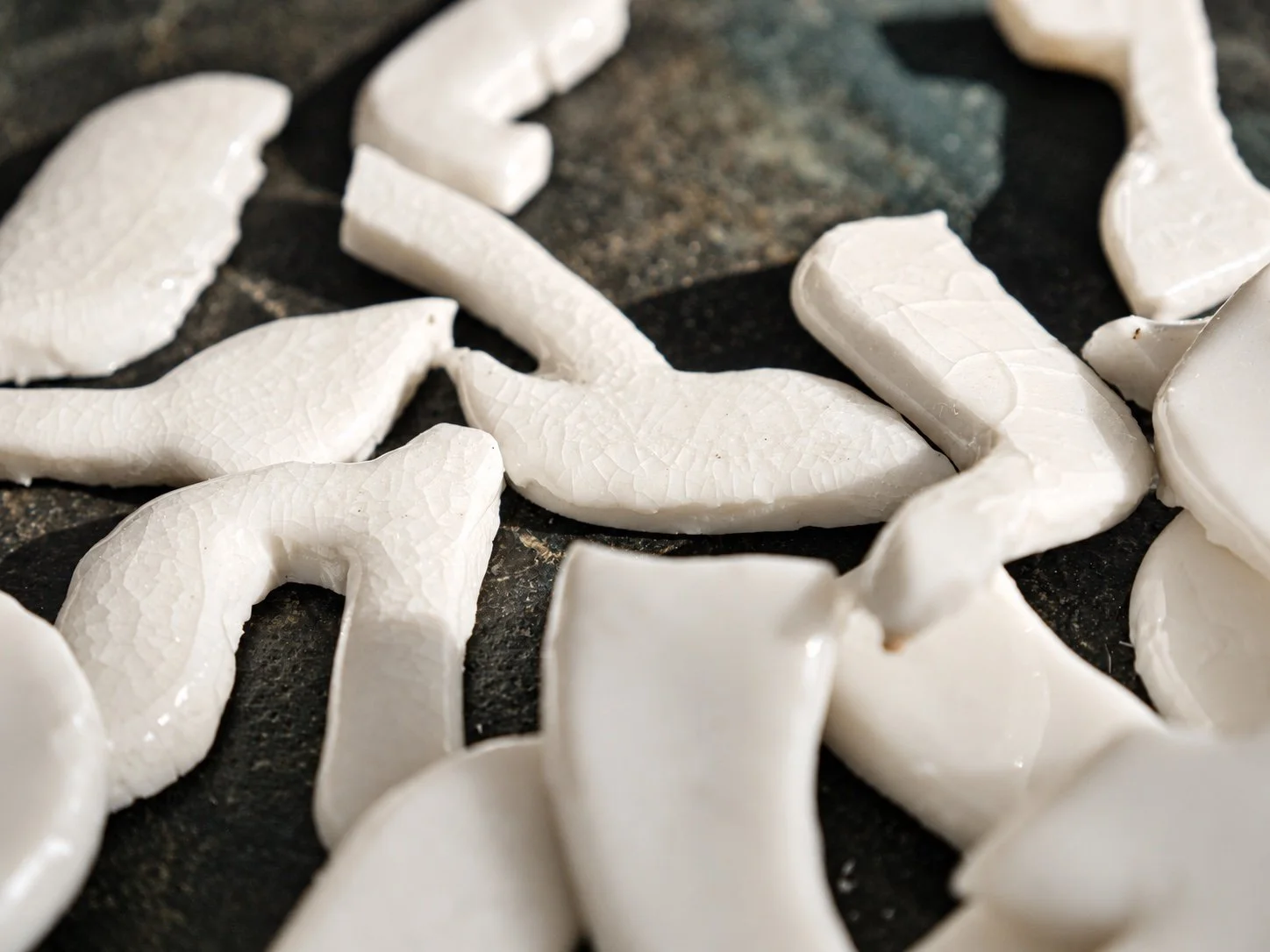Close view of white porcelain letter fragments with a crackled glaze on a dark table top.