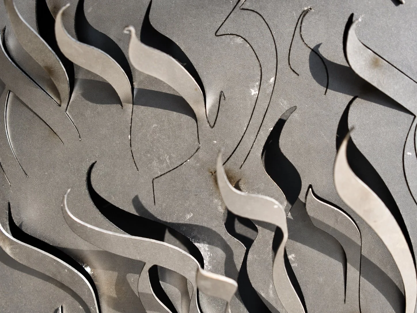 Close view of Hebrew letter forms cut and bent out of a steel surface, casting shadows.