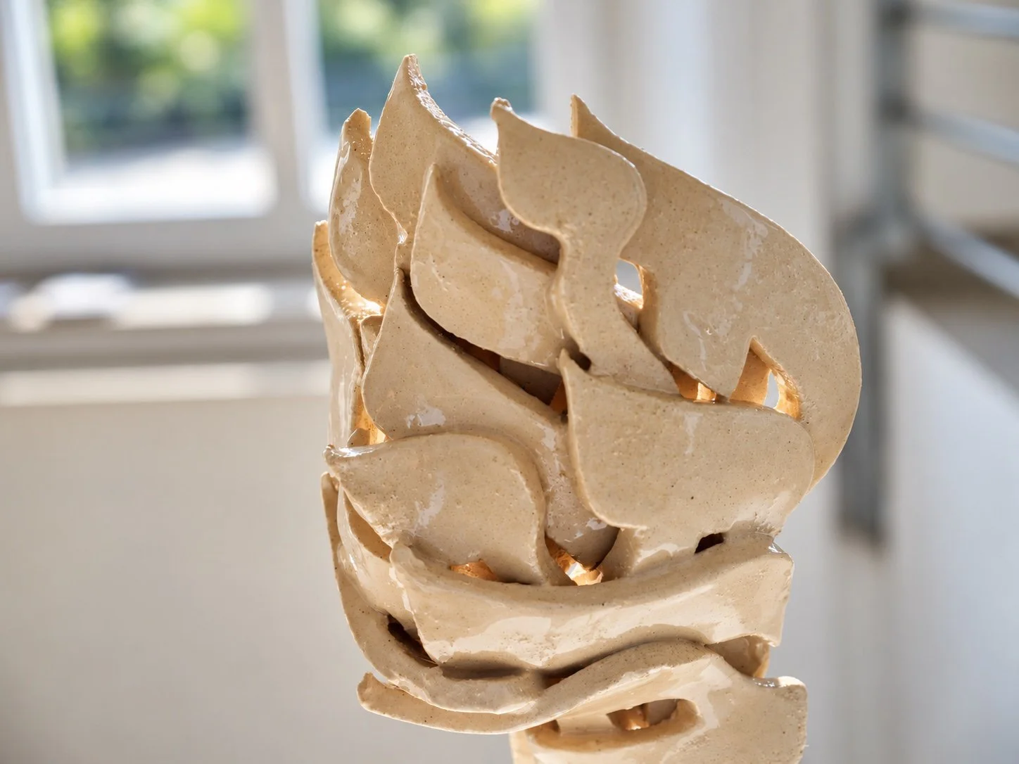 Close view of a ceramic sculpture of layered letter forms lit from behind, with a window in the background.