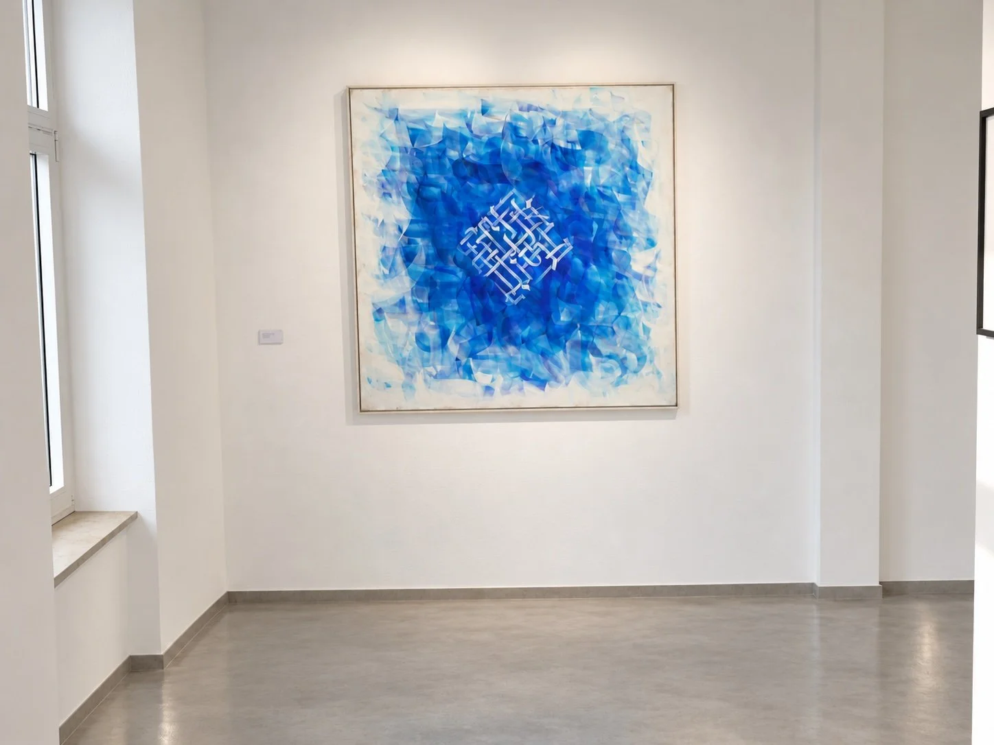 A square painting on canvas with a lattice-like white form at the centre of layered blue brushwork, hung in a white corner of the gallery.