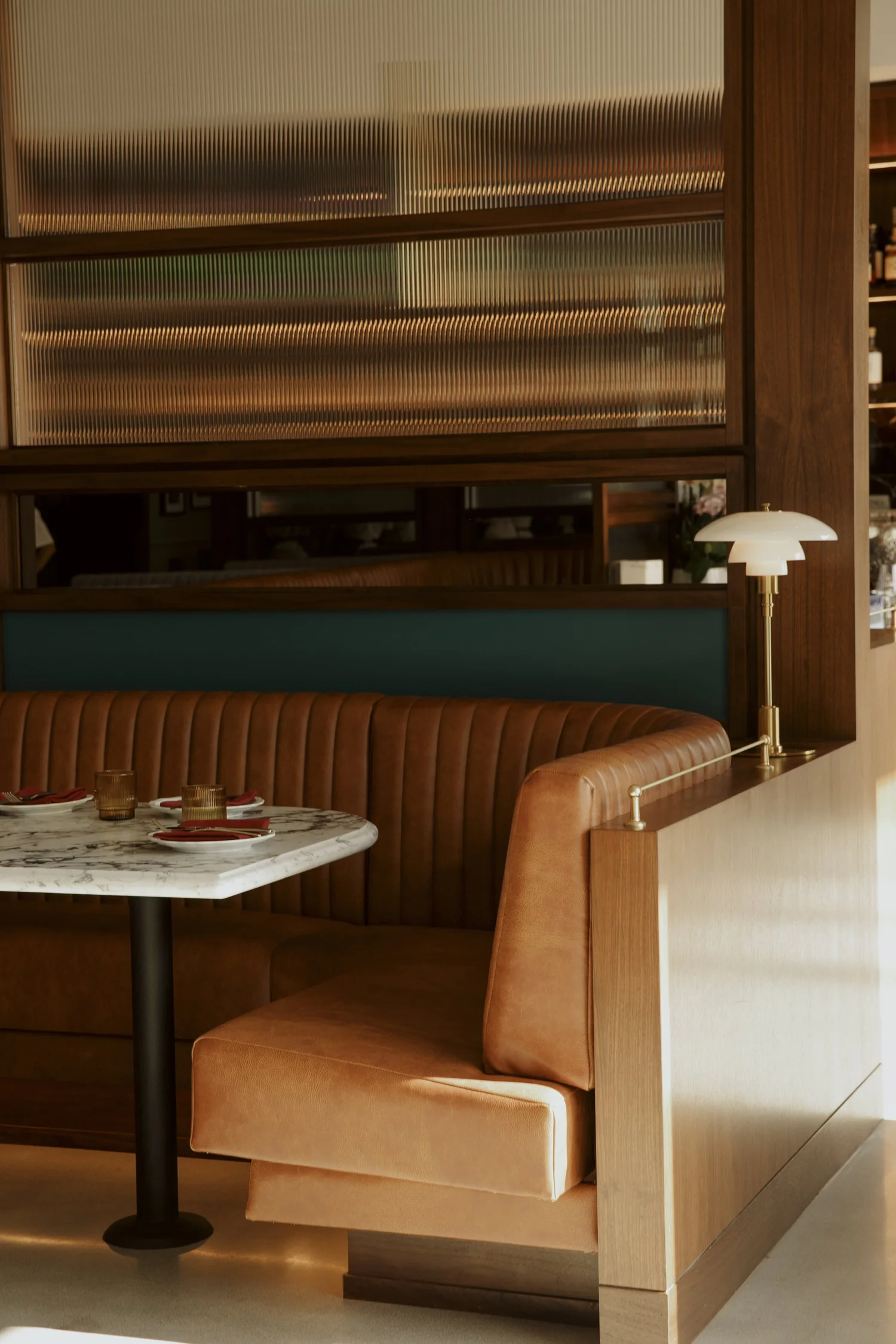 A cognac leather booth at Salina, lit by a brass lamp, with a marble table set with crimson napkins