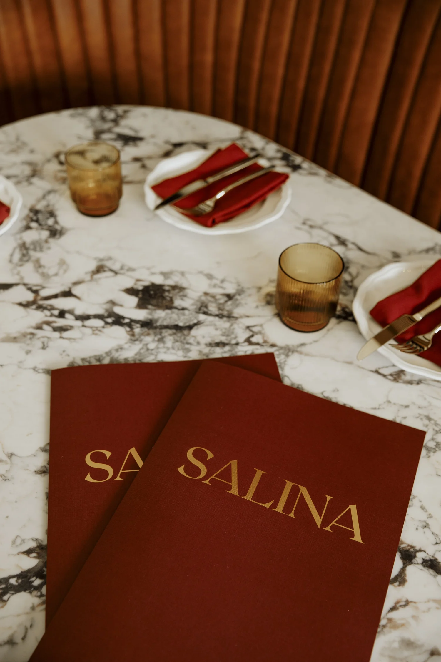 Gold Salina menus on a white marble table with crimson napkins and amber glassware
