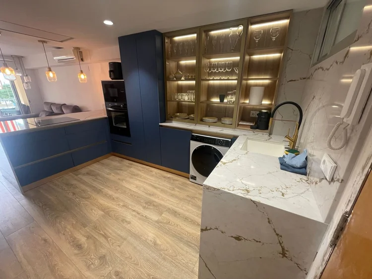 Cocina azul con vitrina iluminada y encimera efecto mármol con veta dorada