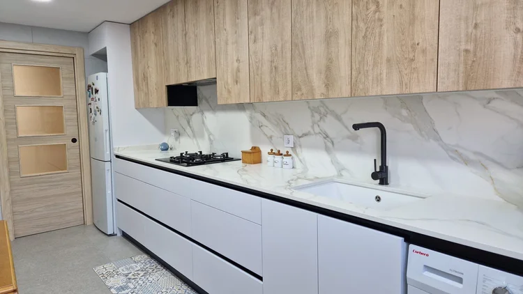 Cocina lineal blanca con muebles altos de madera y frontal efecto mármol