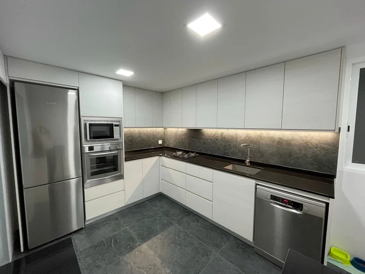 Cocina blanca en L con encimera negra y frontal efecto piedra