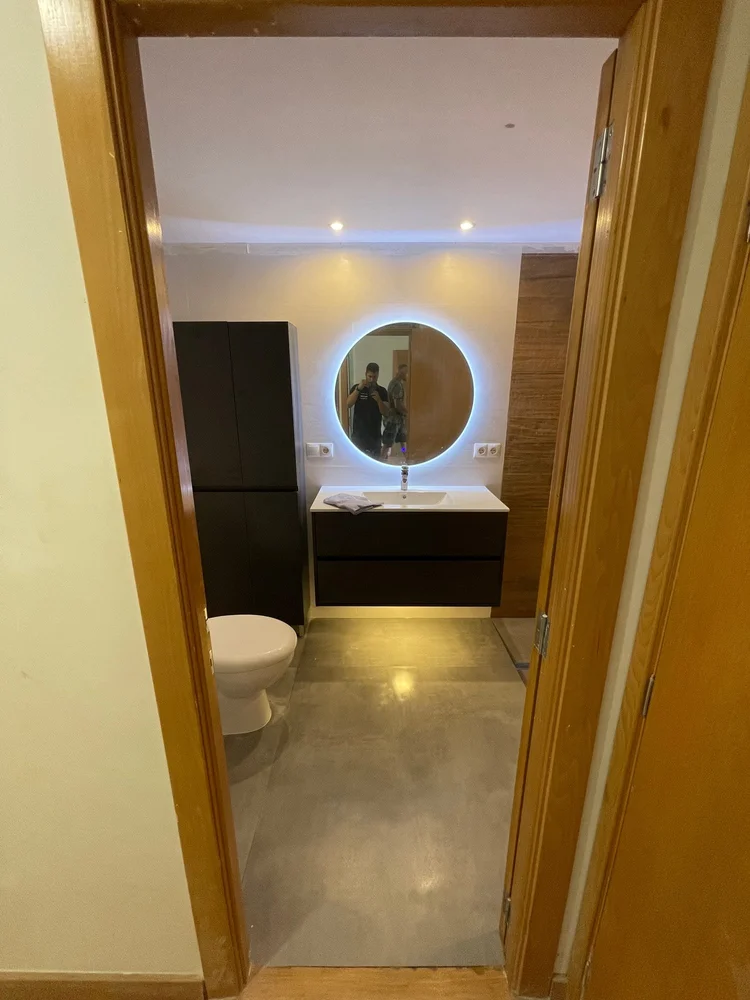 Baño con mueble negro suspendido y espejo circular retroiluminado