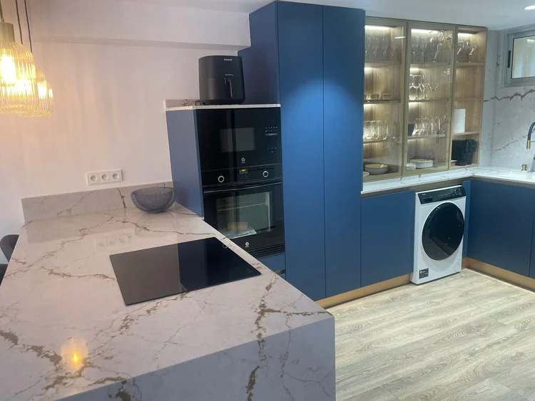Encimera efecto Calacatta dorado y muebles azules con columna de hornos