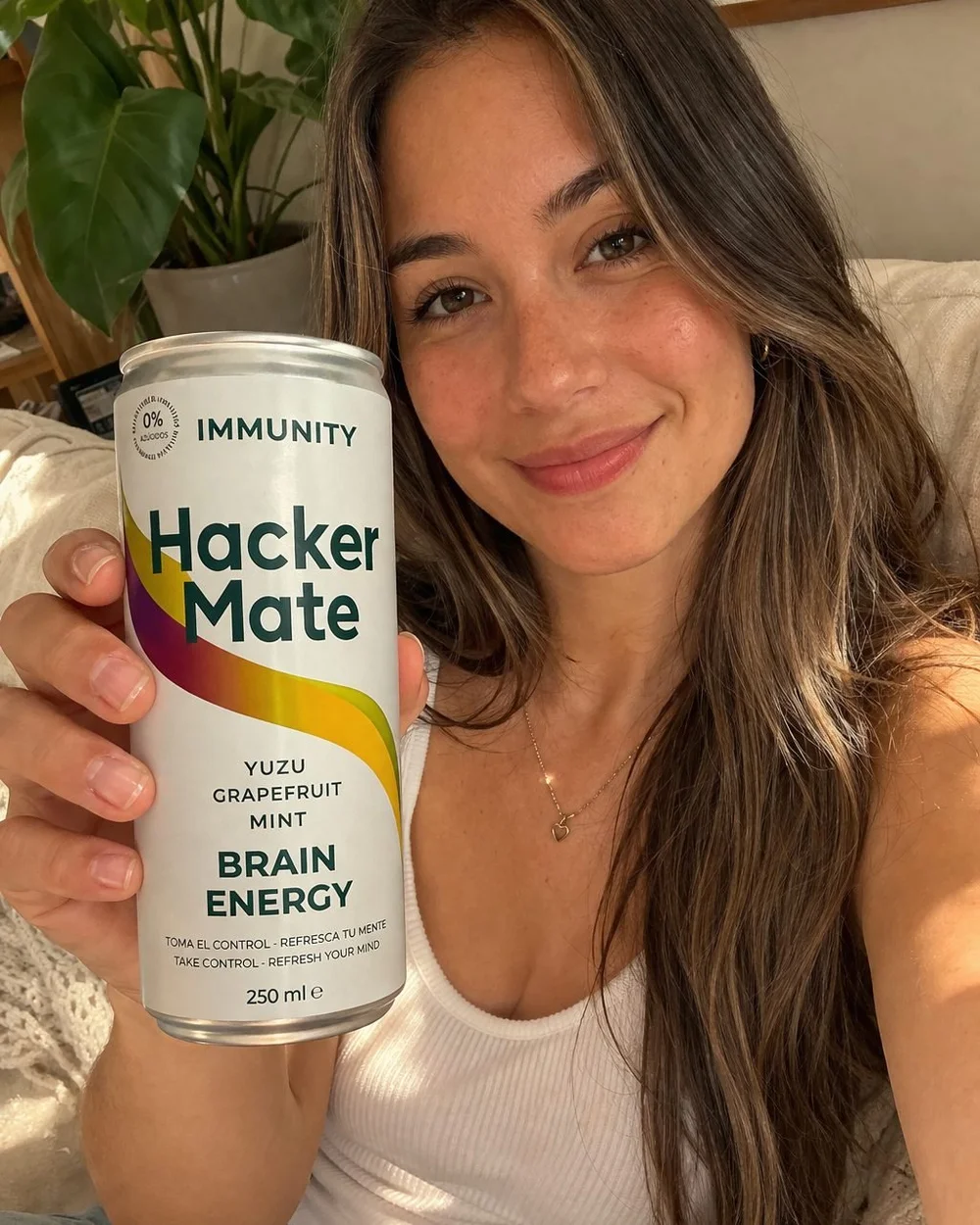 Mujer sonriente sosteniendo una lata de Hacker Mate Immunity en casa