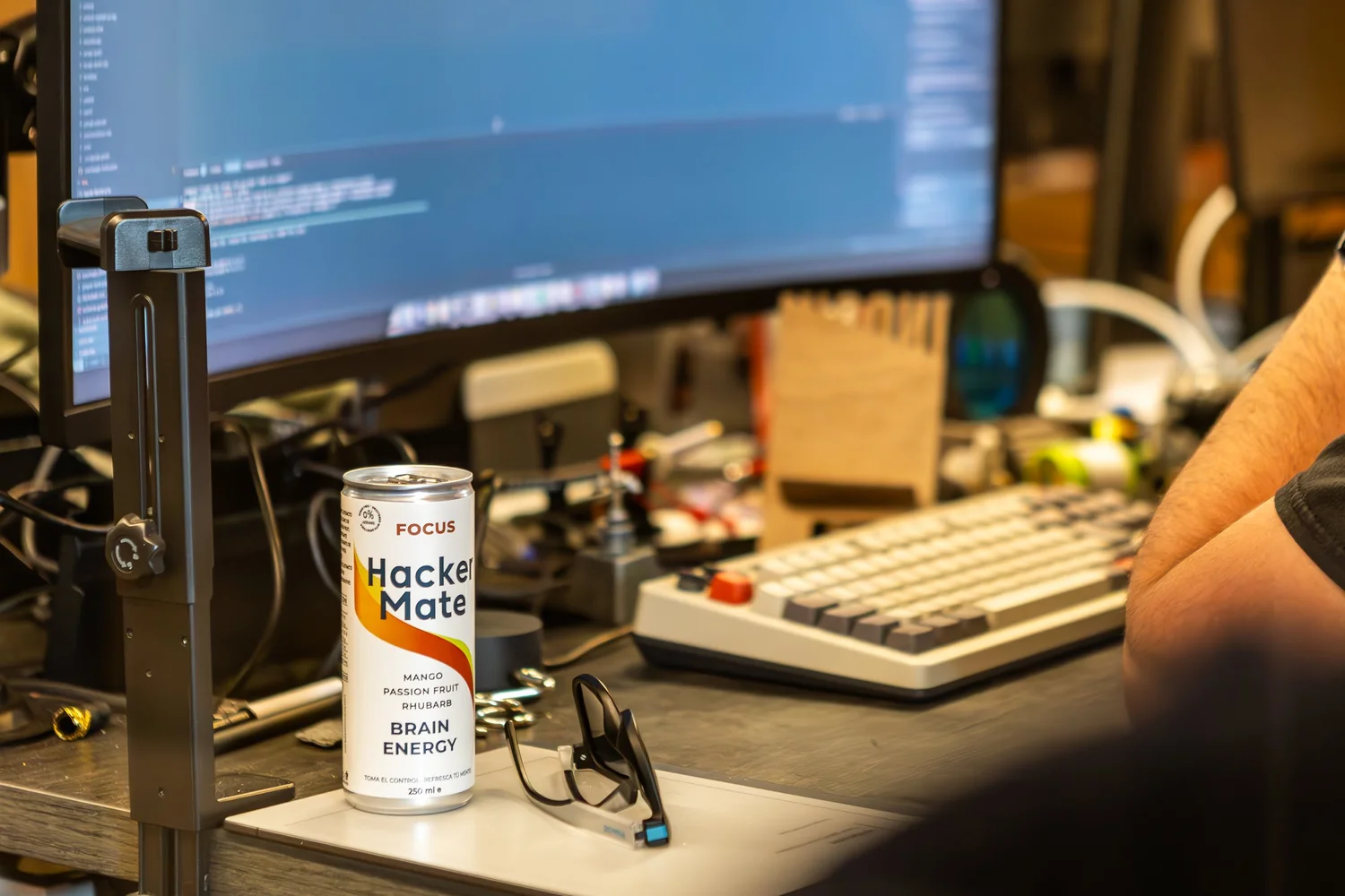 Can of Hacker Mate Focus on a desk next to a keyboard and a screen full of code
