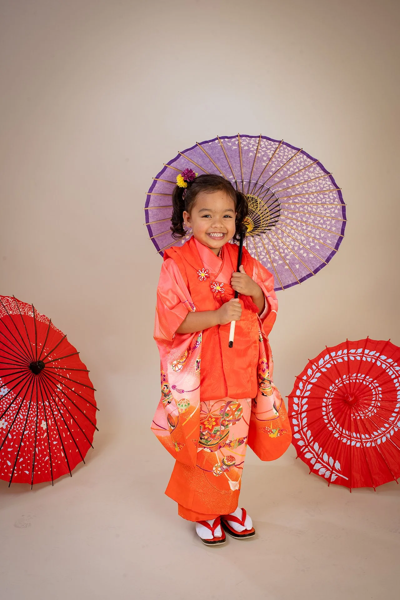 Child in a coral kimono holding a purple Japanese parasol
