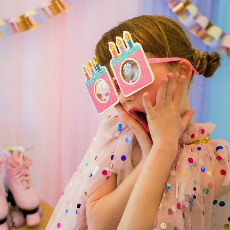 Smiling child in heart-shaped sunglasses and polka dot shirt on pink background