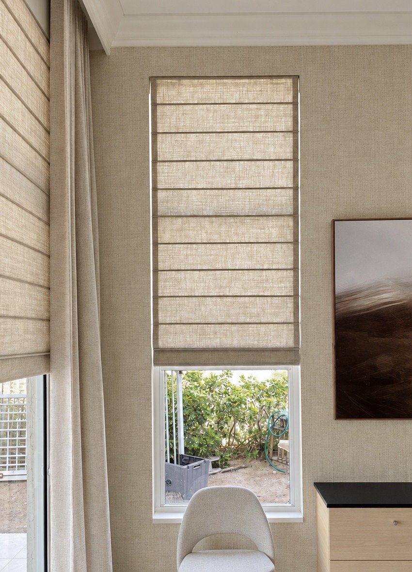 Textured neutral Roman shades on tall windows beside floor-length drapery