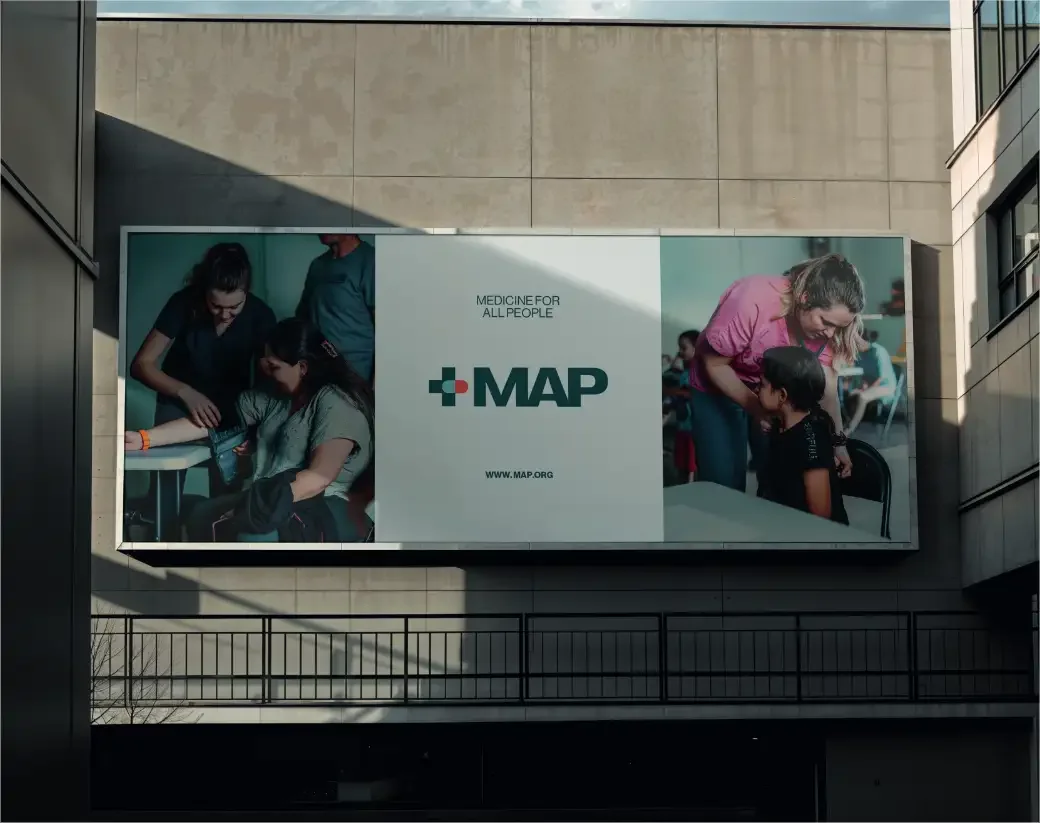 A large MAP banner on a building wall: the new cross and capsule logo between photos of health workers caring for patients