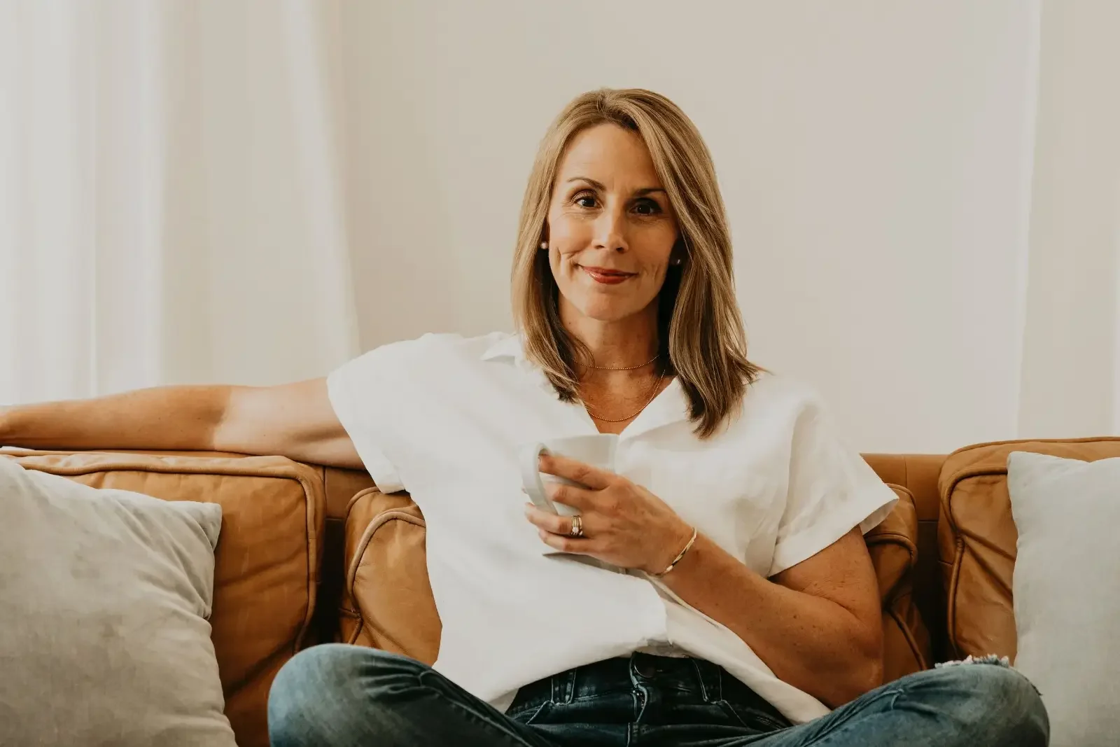 Alli Patterson sitting on a leather couch in a white shirt, smiling at the camera
