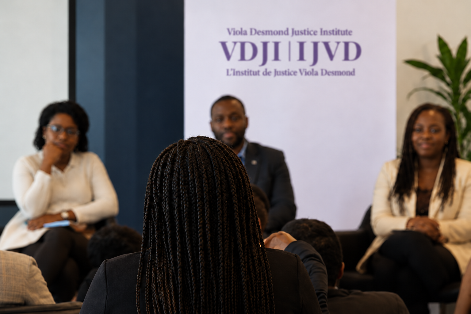 A community discussion, viewed from behind a participant, with a Viola Desmond Justice Institute banner.