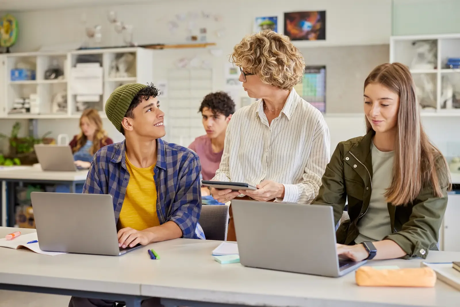 Teacher guiding teen students working on laptops in a bright classroom — Aprise Learning small-group coding instruction