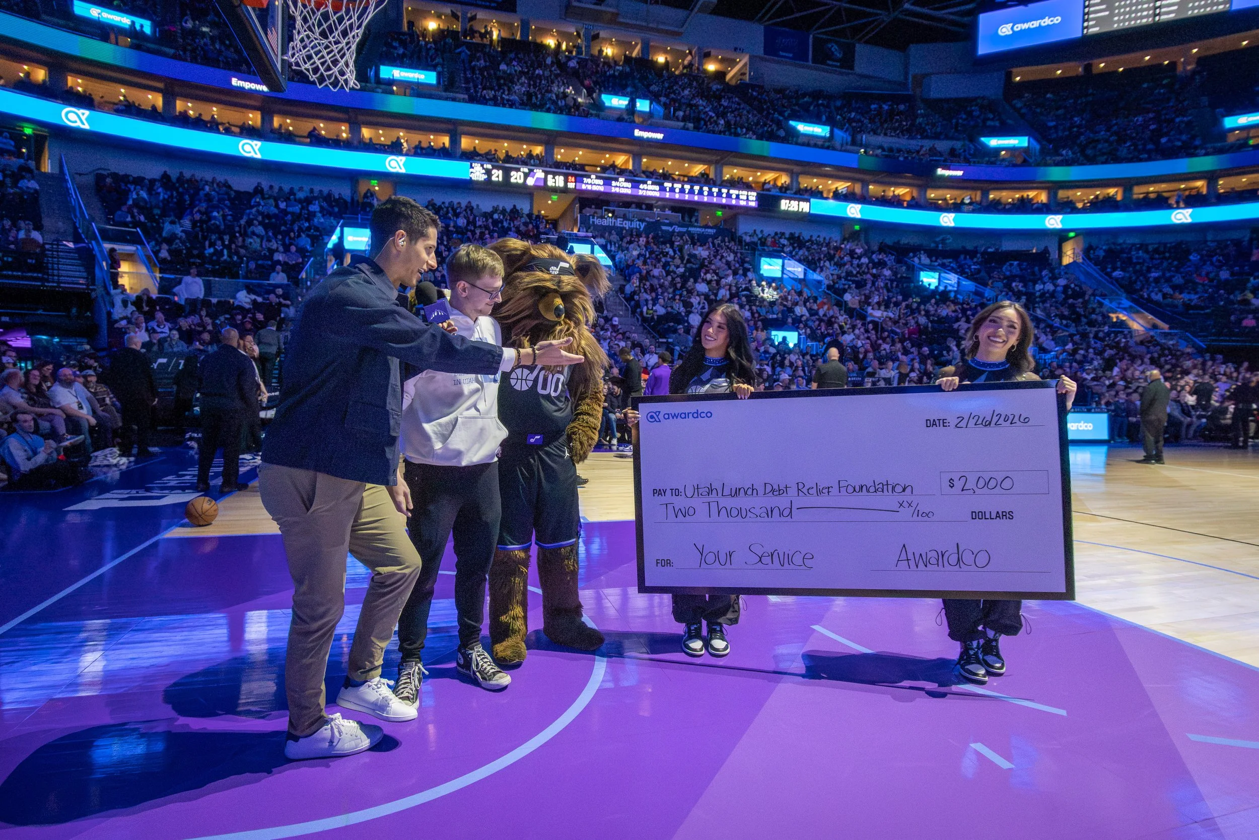 Founder receiving a $2,000 check for the Utah Lunch Debt Relief Foundation on the court at a Utah Jazz game.