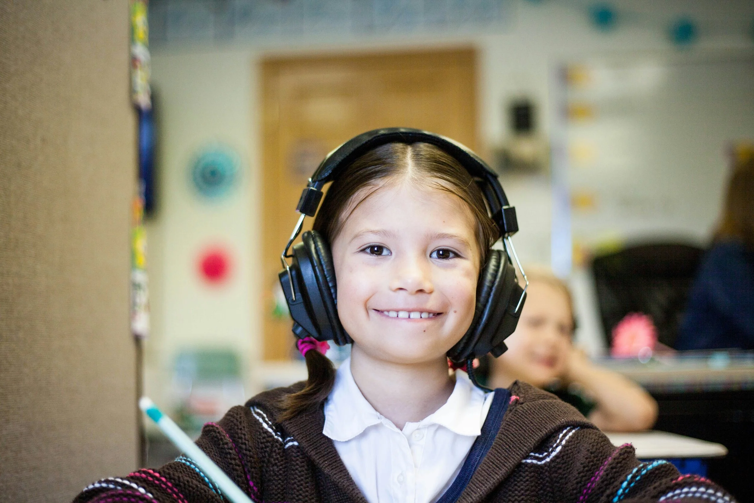 A smiling elementary student wearing headphones in a classroom.