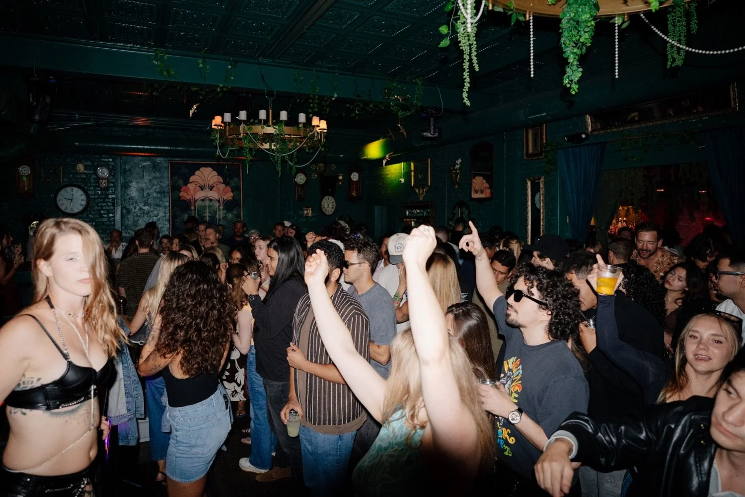 A full dance floor beneath chandeliers and greenery at Mockingbird in Denver.