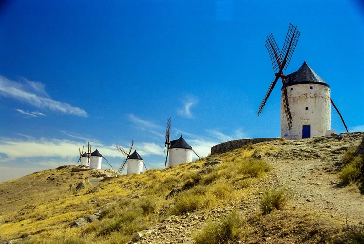 White windmills on a hillside in Spain under a blue sky