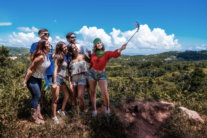 A group of guests stand with El Yunque in the background as they smile and wave for the camera