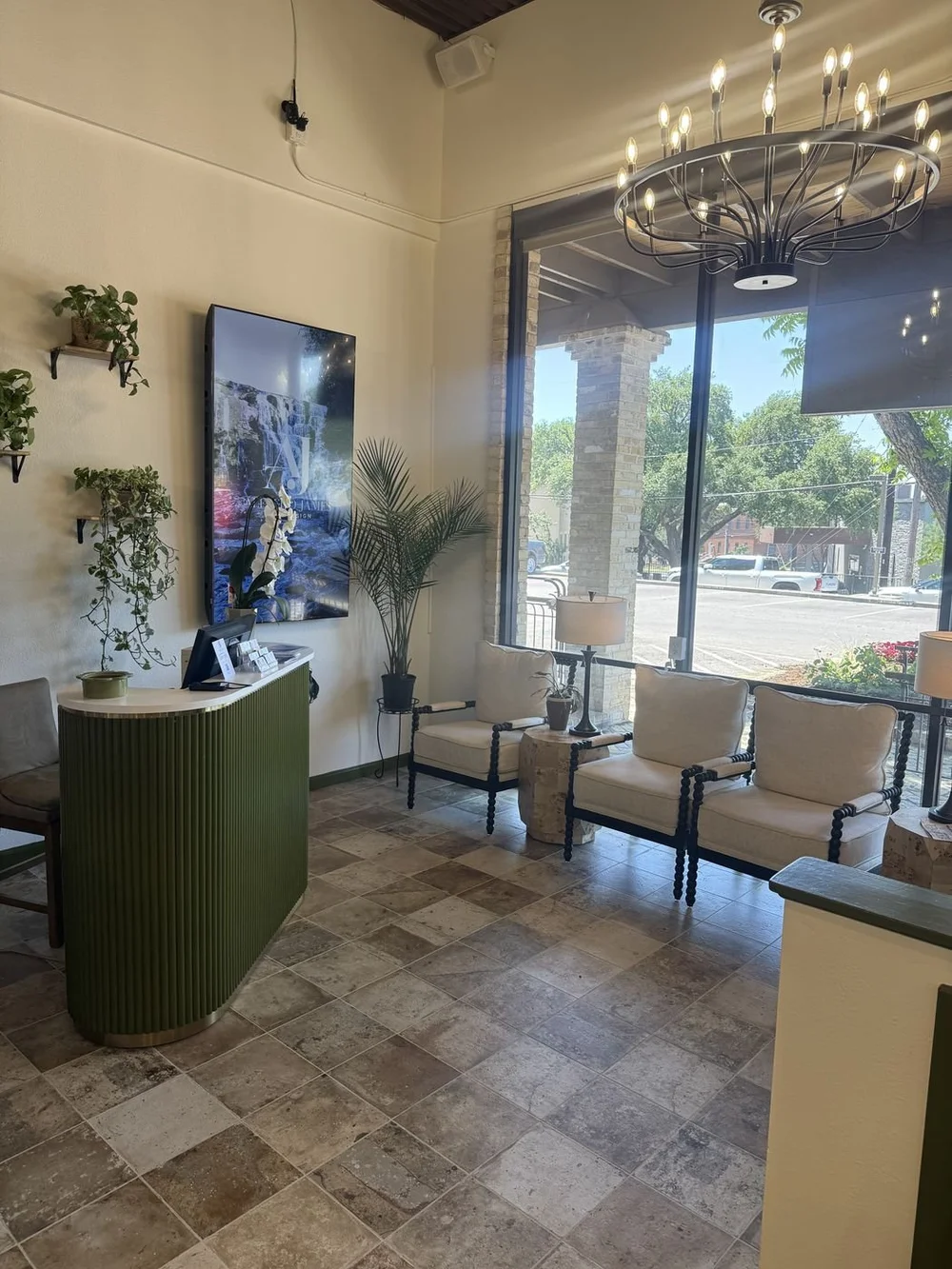 The bright reception and lounge at the Alfredo James Alamo Heights salon, with a chandelier and a green fluted front desk