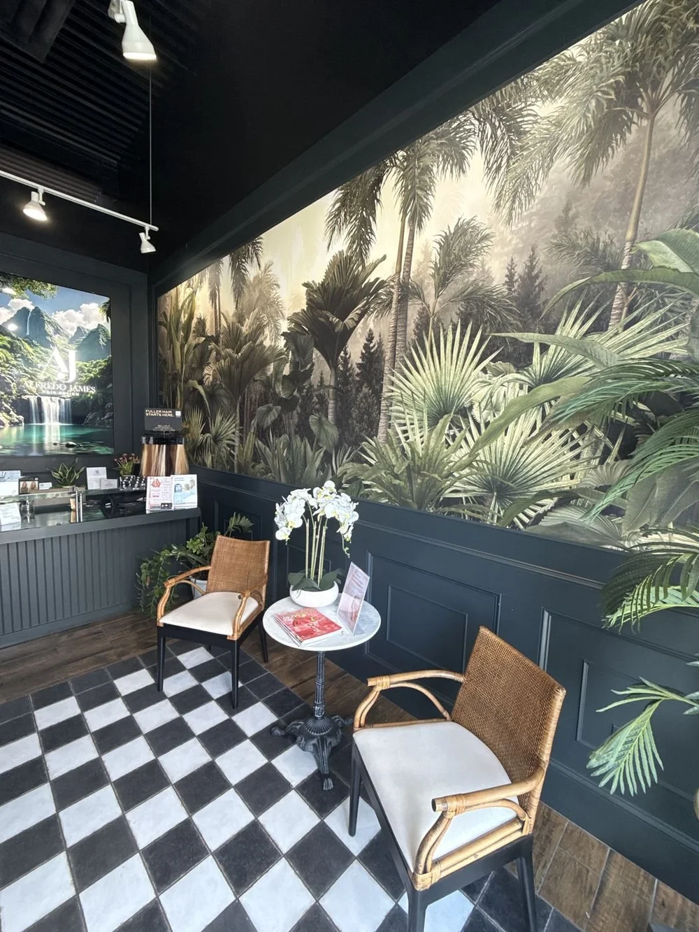 The guest lounge at the Alfredo James Stone Oak salon, with a jungle mural, rattan chairs and a checkered floor
