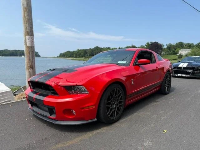 A red Shelby GT500 with black stripes parked beside the water