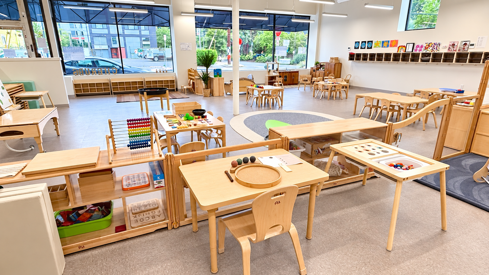 Seattle classroom with child-sized wooden tables, open learning shelves, and windows.